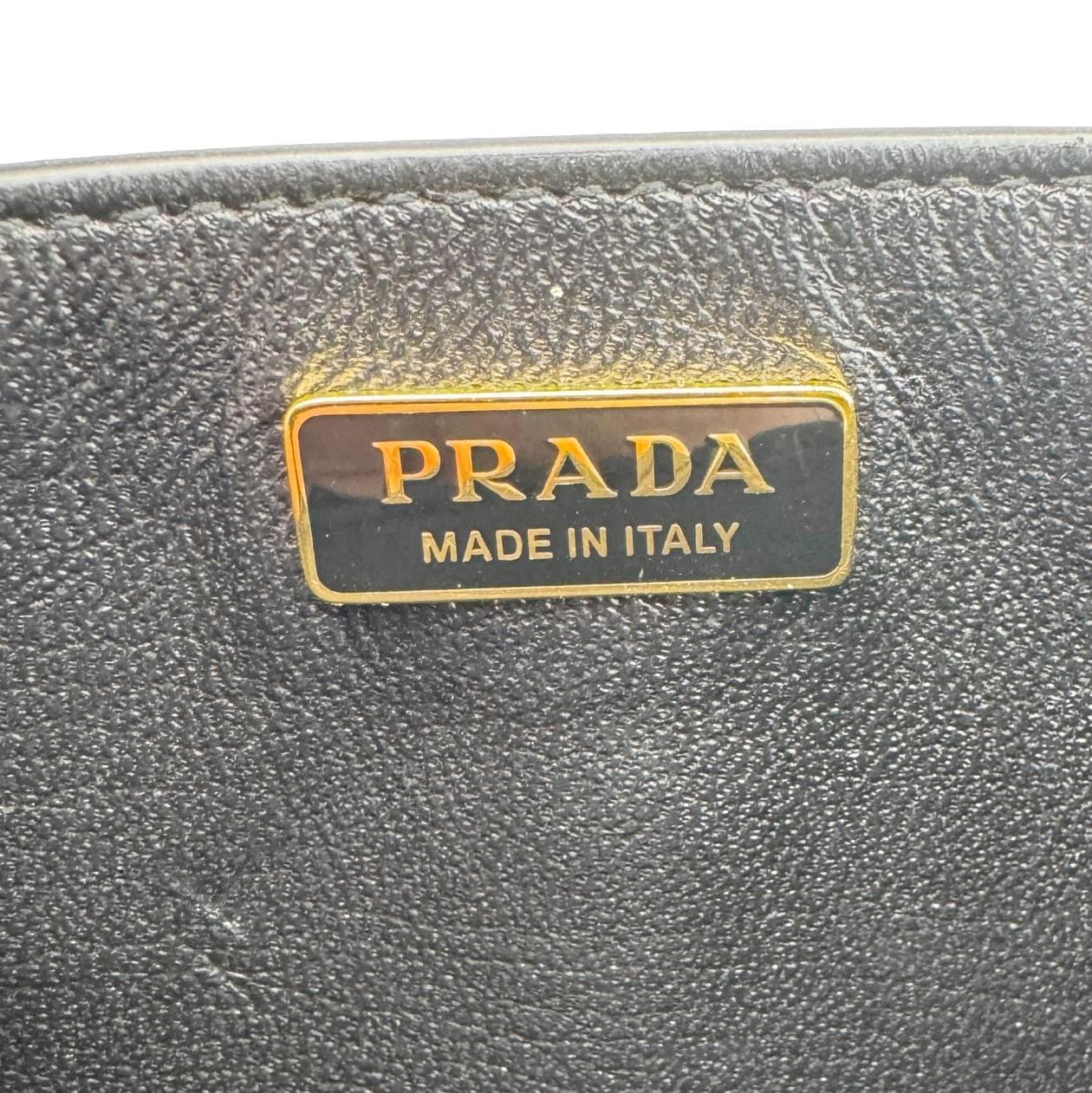 Close-up of gold PRADA Made in Italy logo on Saffiano Lux leather of PRADA Saffiano Lux Chain Crossbody Bag Black.