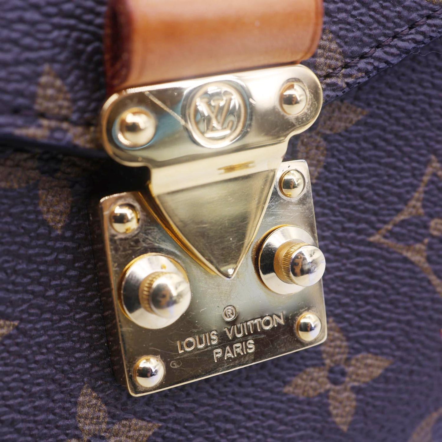 Close-up of the LOUIS VUITTON Lovelock Metis Pochette Patches Monogram Canvas Crossbody Bag Brown clasp detail.